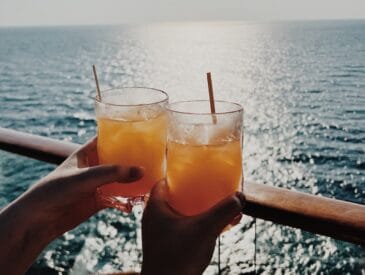 Two people hold their cocktail overlooking the ocean