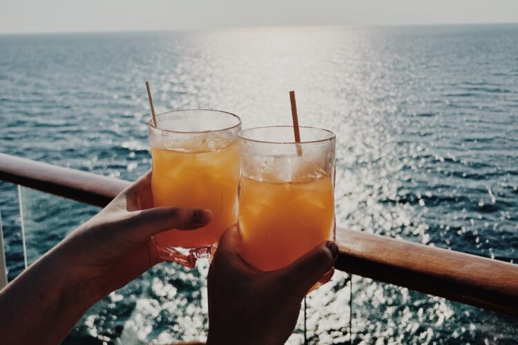 Two people hold their cocktail overlooking the ocean