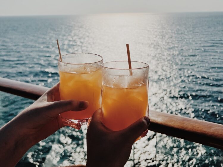 Two people hold their cocktail overlooking the ocean