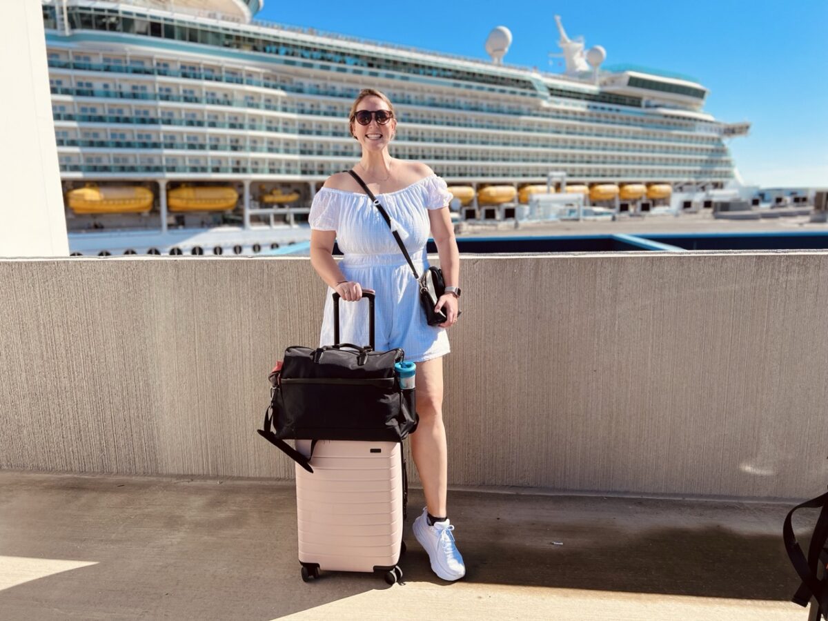Allie stands in front of a cruise ship and smiles with her luggage in hand