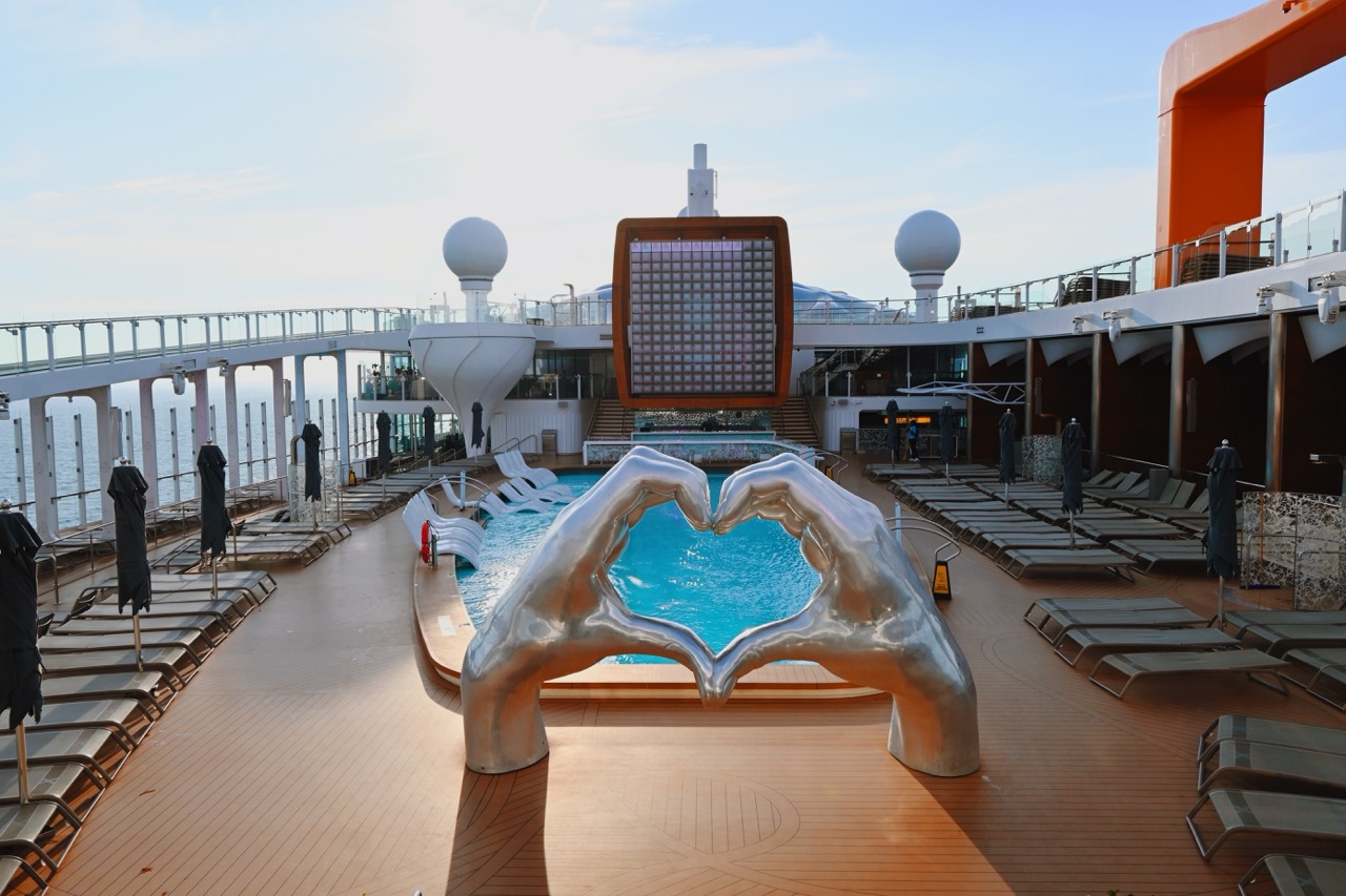 Celebrity Apex pool deck at sunset with heart hands